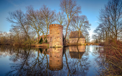 Reflection of bare trees in moat of a castle against sky