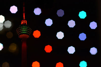 Illuminated lantern hanging against colorful lights at night