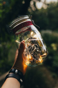 Cropped image of hand holding glass jar with illuminated lights