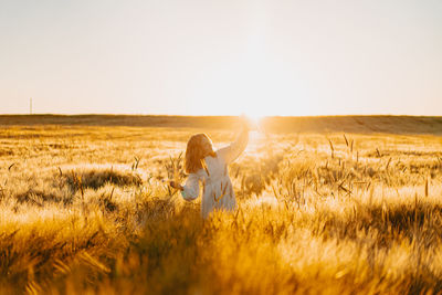 Woman standing on field against sky during sunset