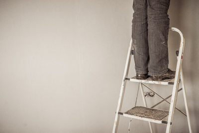 Low section of man standing on ladder against wall
