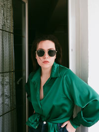 Portrait of young woman wearing sunglasses against wall