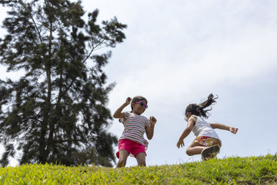 Low angle view of sisters playing on grass against sky