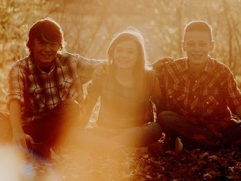 Portrait of siblings smiling while sitting on field during sunset