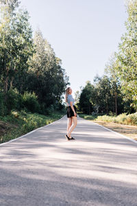 Woman on road amidst trees against sky