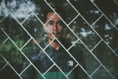 Portrait of man seen through wet window