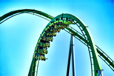 Low angle view of people enjoying rollercoaster against blue sky