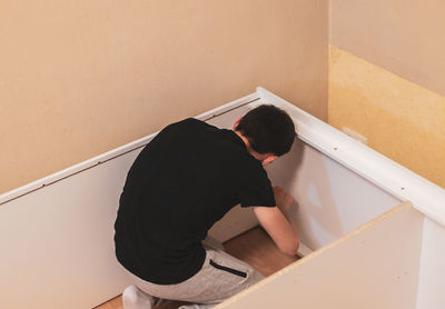 A young man is screwing a screw into a board with a screwdriver.