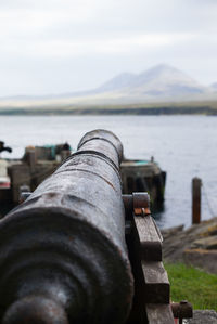 Close-up of metal by river against sky
