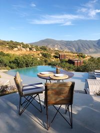 Chairs and tables at swimming pool against sky