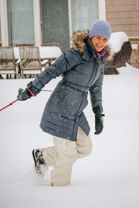 Portrait of smiling woman wearing warm clothing walking on snow during snowfall