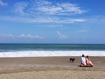 Women sitting on beach against sky