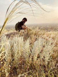 Side view of man sitting on field against sky