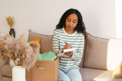 African-american female keeping count for clothing in cardboard box. moving away and packing