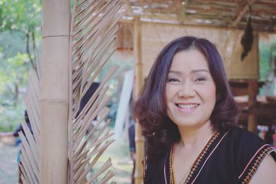 Close-up portrait of mature woman smiling while standing by bamboo