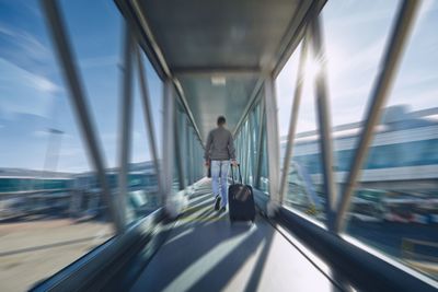 Rear view of man walking in passenger boarding bridge at airport