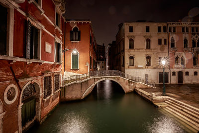 Bridge over canal amidst buildings in city at night