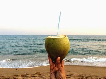 Close-up of hand holding drink at beach against sky