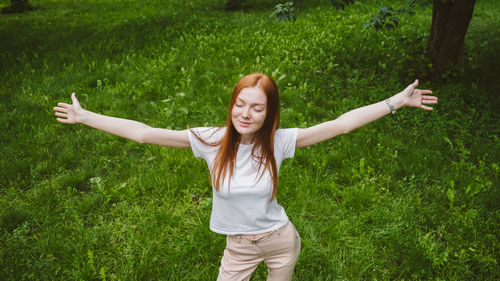Happy young woman with arms raised on field