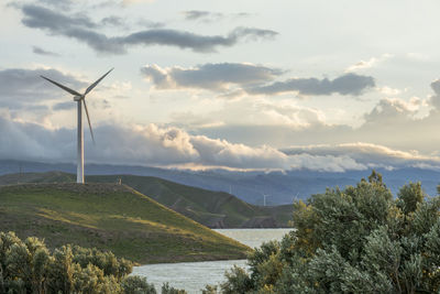 Wind power turbine on hill in front of cloudy sky