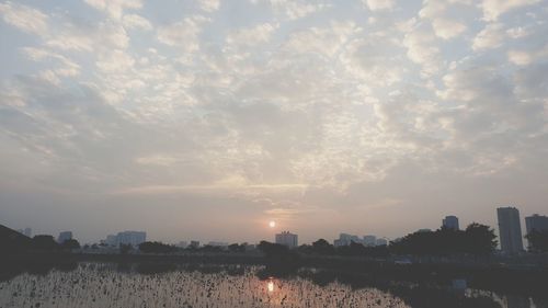 Scenic view of river by buildings against sky during sunset