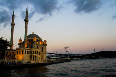 Mosque by strait against cloudy sky during sunset