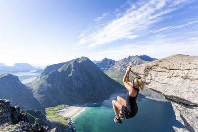 Mid adult woman hanging on edge of mountain at ryten, lofoten, norway