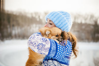Woman with puppy standing on snow against sky during winter