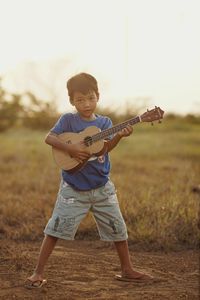 Full length of boy standing on field playing ukulele
