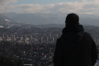 Rear view of woman looking at cityscape against sky