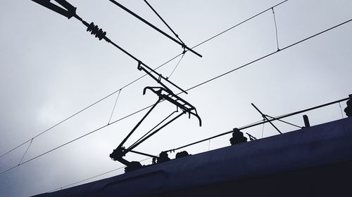 Low angle view of silhouette birds perching on cable against sky