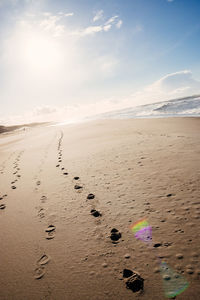 Footprints on sand at beach against sky