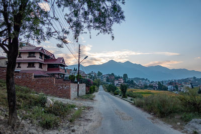 Road amidst trees and buildings against sky