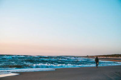 Woman walking on beach against clear sky