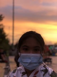 Portrait of girl wearing mask against orange sky