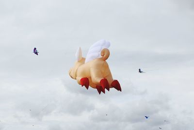 Low angle view of inflatable pig toy flying against sky