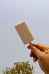 Hand holding ice cream cone against sky