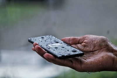 Cropped hand of person holding phone in rain