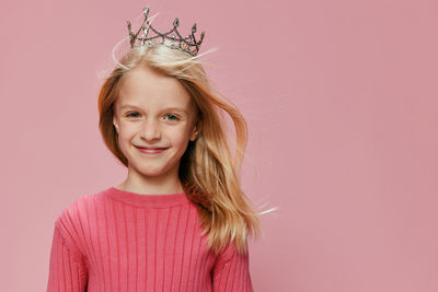 Portrait of young woman standing against pink background