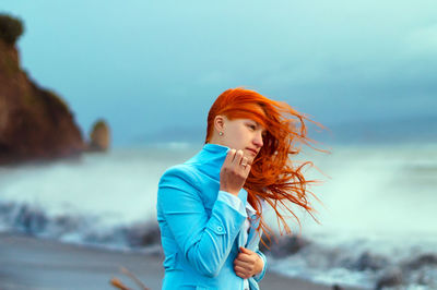Young woman standing at beach against sky