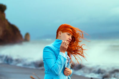 Young woman standing at beach against sky