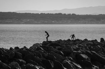 Silhouette man standing on rock by sea against clear sky