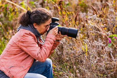 Side view of an attractive woman with professional dslr camera in meadow photographing wild flowers