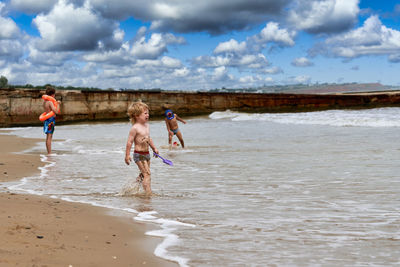 Children playing at beach against sky