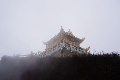 Low angle view of golden summit temple against sky during foggy weather