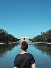 Rear view of man looking at lake against sky