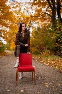 Portrait of a young woman with old armchair in a brown coat in autumn