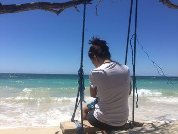 Rear view of man on rope at beach against clear sky