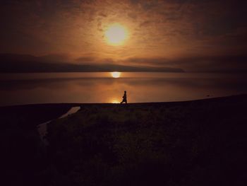 Silhouette man standing on shore against sky during sunset