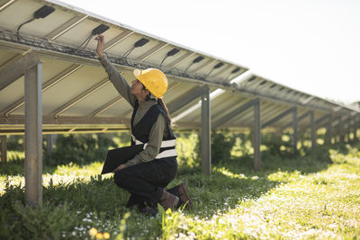 Female engineer fixing connection of solar panels while kneeling at power station